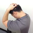 耳の後ろで手を組み、下を向く